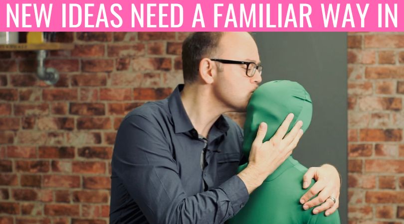 A man kisses a green figure beneath the headline “New Ideas Need A Familiar Way In,” representing the mix of familiarity and surprise.